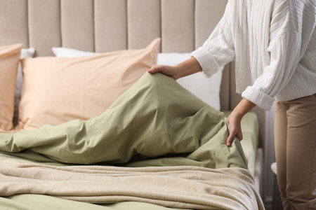 Woman making bed with new pistachio linen in room, closeupの写真素材