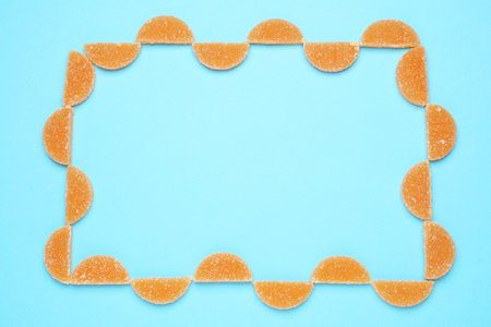 Frame made with orange marmalade candies on light blue background, flat lay. Space for textの写真素材