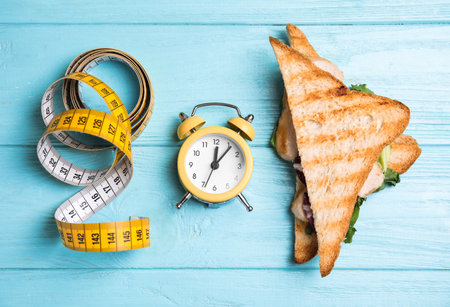Tasty sandwich, alarm clock and measuring tape on light blue wooden table, flat lay. Diet regimenの写真素材
