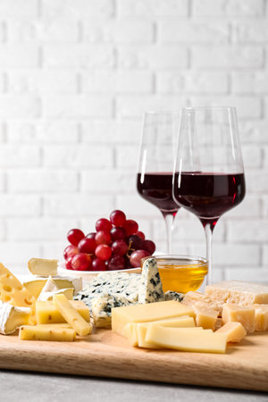 Cheese plate with honey, grapes and nuts on gray table, against brick wallの写真素材