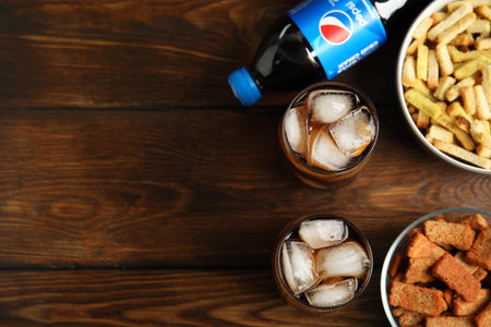 MYKOLAIV, UKRAINE - FEBRUARY 15, 2021: Glasses and bottle of Pepsi with snacks on wooden table, flat lay. Space for textのeditorial素材