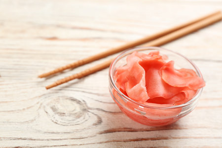 Spicy pickled ginger and chopsticks on white wooden table, closeup. Space for textの写真素材
