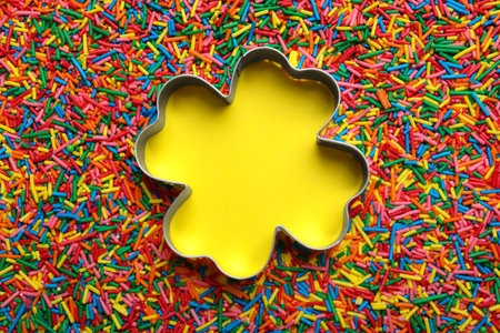 Clover shaped cookie cutter and sprinkles on yellow background, flat lay with space for text. Confectionery decorの写真素材