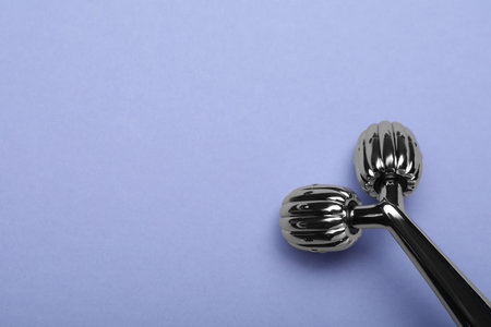 Metal face roller on lilac background, top view. Space for textの写真素材