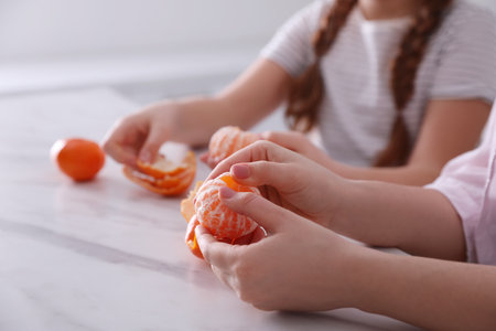 Girls peeling fresh tangerines at table in kitchen, closeupの写真素材