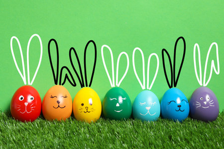 Colorful eggs as Easter bunnies on green grass against color backgroundの写真素材