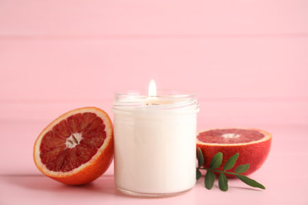 Scented candle with burning wooden wick and cut grapefruit on pink tableの写真素材