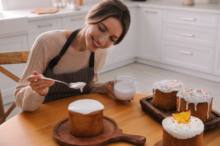 Young woman decorating traditional Easter cake with glaze in kitchenの写真素材