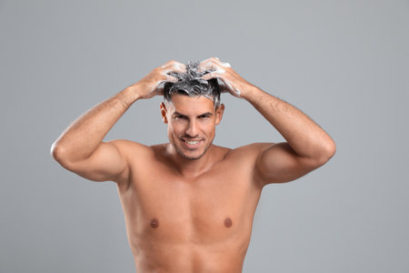 Handsome man washing hair on gray backgroundの写真素材