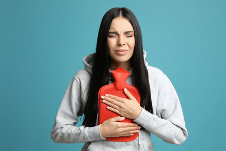 Woman using hot water bottle to relieve pain on light blue backgroundの写真素材