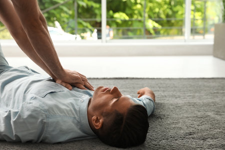 Passerby performing CPR on unconscious man indoors. First aidの写真素材