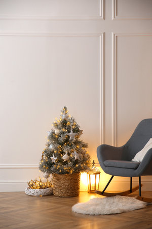 Beautiful Christmas tree, lantern and rocking chair near wall in roomの写真素材