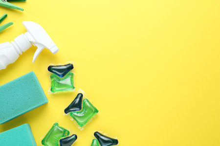 Laundry capsules, spray bottle and sponges on yellow background, flat lay. Space for textの写真素材