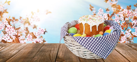 Basket with traditional Easter cake and eggs on wooden table outdoors, space for text. banner designの写真素材