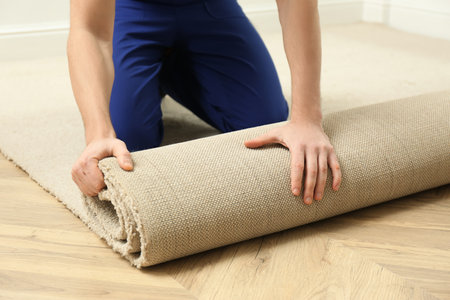 Worker rolling out new carpet flooring indoors, closeup