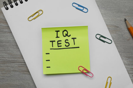 Sticky paper with words IQ Test, notebook and fasteners on wooden table, flat layの写真素材