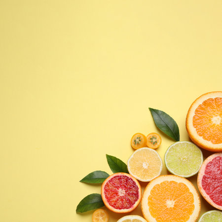 Fresh juicy citrus fruits with green leaves on light yellow background, flat lay. Space for textの写真素材