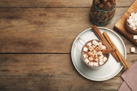 Glass cup of hot cocoa with aromatic cinnamon and marshmallows on wooden table, flat lay. Space for textの写真素材
