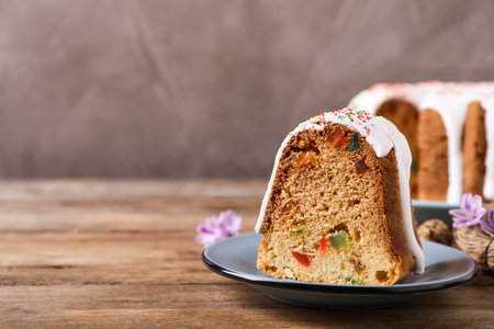 Piece of glazed Easter cake with sprinkles and candied fruits on wooden table, space for text