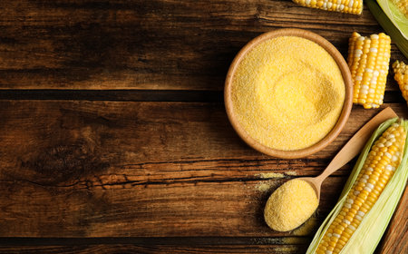 Flat lay composition with cornmeal and fresh cobs on wooden table, space for textの写真素材