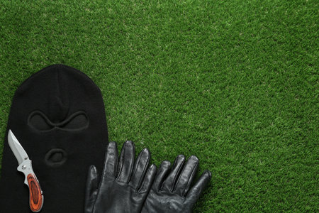 Black knitted balaclava, gloves and knife on green grass, flat lay. Space for textの写真素材