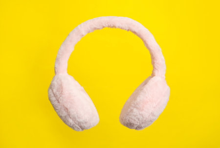 Fluffy earmuffs on yellow background. Stylish winter accessoriesの写真素材