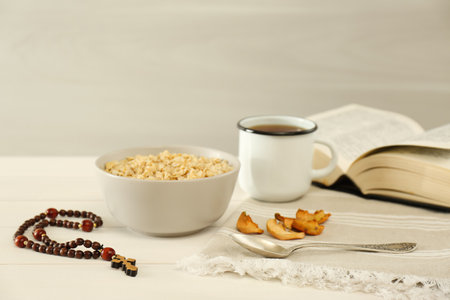 Rosary beads, oatmeal porridge, dried apples, drink and Bible on white wooden table. Lent seasonの写真素材