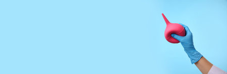 Doctor holding pink enema on light blue background, closeupの写真素材