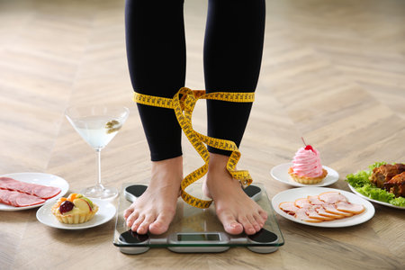 Food, alcohol left after holidays and woman with measuring tape standing on scales indoors, closeup. overweight problemの写真素材