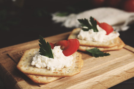 Delicious crackers with cream cheese, tomato and parsley on wooden board, closeupの写真素材