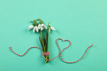 Beautiful snowdrops with traditional cord martisor on turquoise background, flat lay. Symbol of first spring dayの写真素材