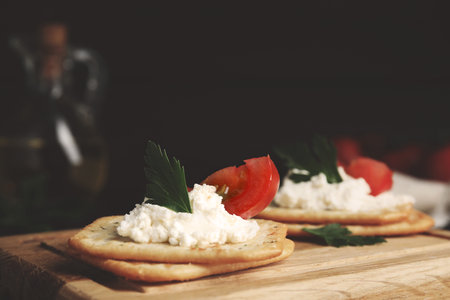 Delicious crackers with cream cheese, tomato and parsley on wooden board, closeupの写真素材