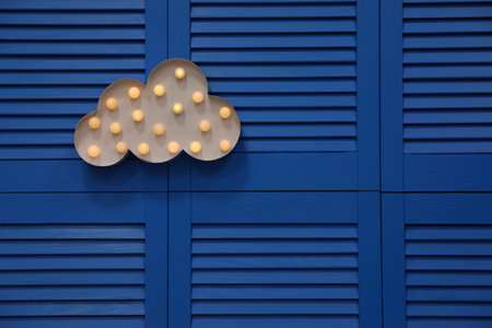 Stylish cloud shaped glowing night lamp hanging on blue folding screen. Space for textの写真素材