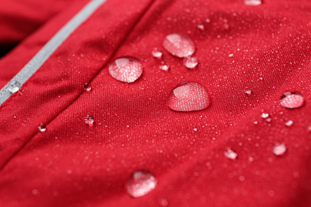 Red waterproof fabric with water drops as background, closeup