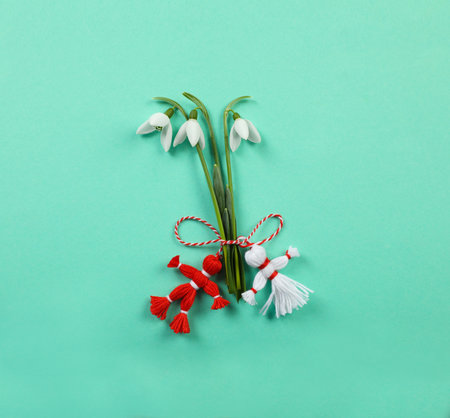 Beautiful snowdrops with traditional martisor on turquoise background, flat lay. Symbol of first spring dayの写真素材