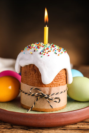 Traditional Easter cake with burning candle on wooden table against black background
