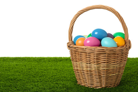 Wicker basket with bright painted Easter eggs on green grass against white background. Space for textの写真素材