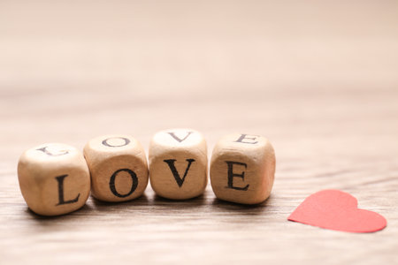 Mini cubes with letters forming word Love near red paper heart on wooden background, closeupの写真素材