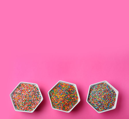 Colorful sprinkles in bowls on pink background, flat lay with space for text. Confectionery decorの写真素材