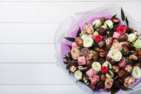 Beautiful bouquet of flowers and chocolate candies on white wooden background, top view. Space for textの写真素材