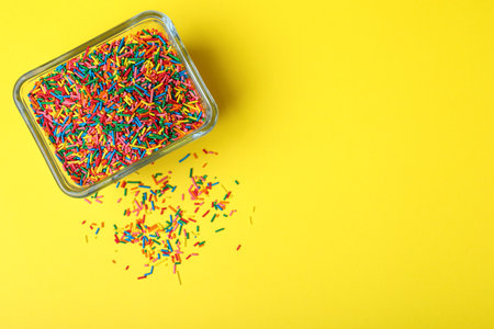 Colorful sprinkles in bowl on yellow background, top view with space for text. Confectionery decorの写真素材