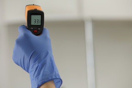 Closeup view of doctor with infrared thermometer on blurred background, space for text. Checking temperature during Covid-19 pandemicの写真素材