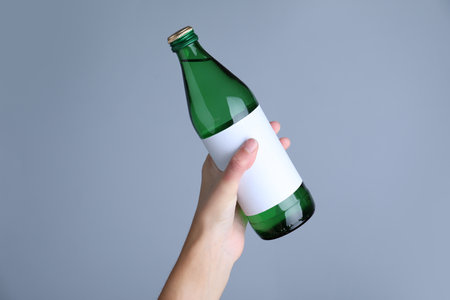 Woman holding glass bottle with soda water on light gray background, closeupの写真素材