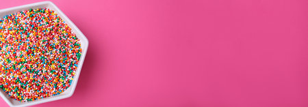 Colorful sprinkles in bowl on pink background, top view with space for text. Confectionery decorの写真素材