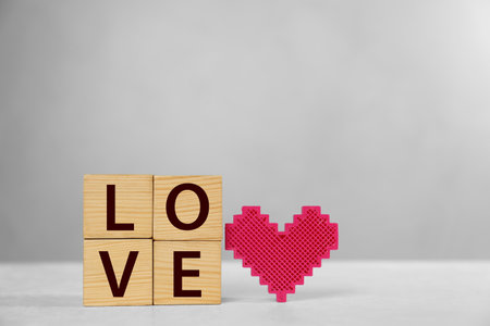 Word Love made of wooden cubes with letters near decorative heart on light tableの写真素材