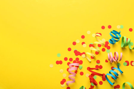 Colorful serpentine streamers and confetti on yellow background, flat lay. Space for textの写真素材