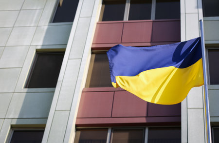 Ukrainian flag near modern building, low angle view