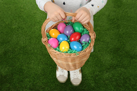 Little girl with basket full of Easter eggs on green grass, closeup
