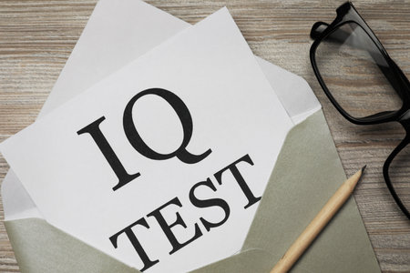 Paper with words IQ Test in envelope, pencil and glasses on wooden table, flat layの写真素材