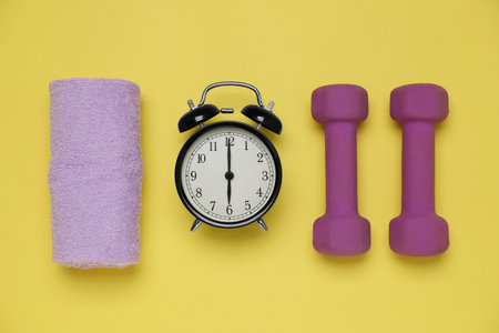 Alarm clock, towel and dumbbells on yellow background, flat lay. morning exerciseの写真素材